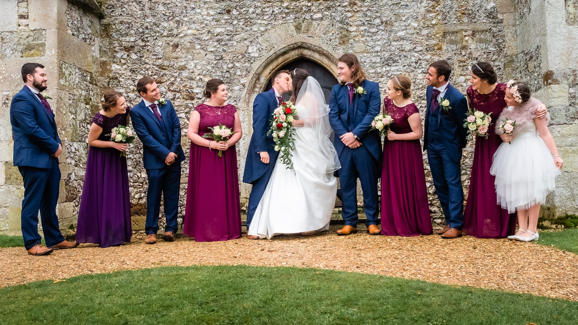 Guests look on as a bride and groom kiss outside an English country church