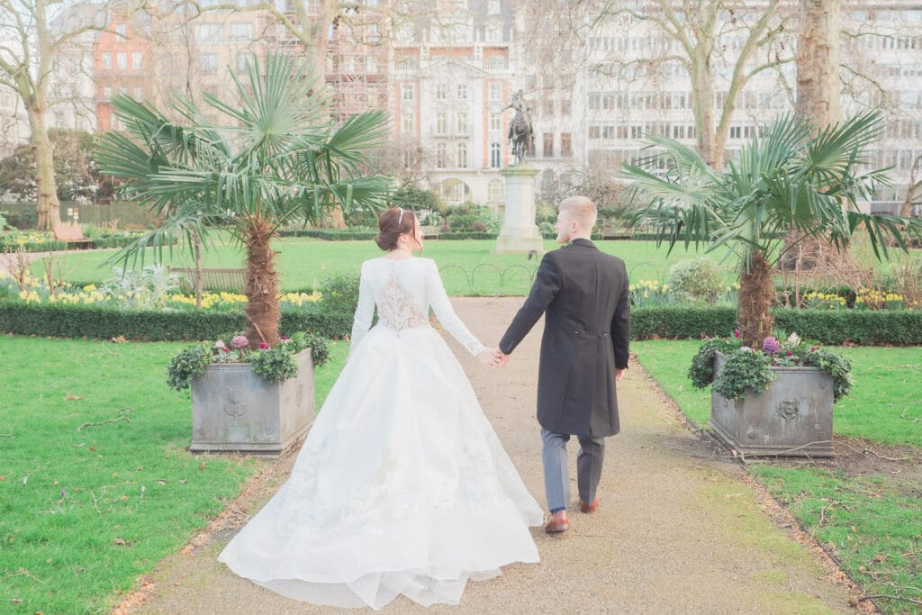 Bride and groom hold hands and walk through St. James's Square, London