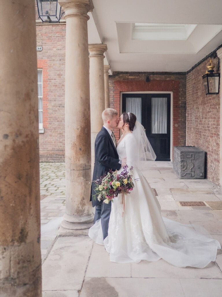 Bride and groom kiss beneath a covered walkway