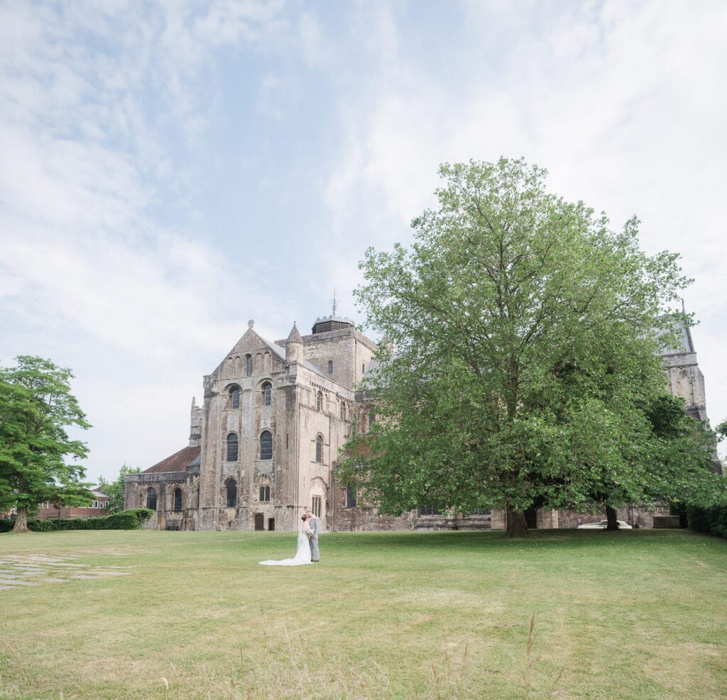 Bride and groom kiss on the green outside Romsey Abbey