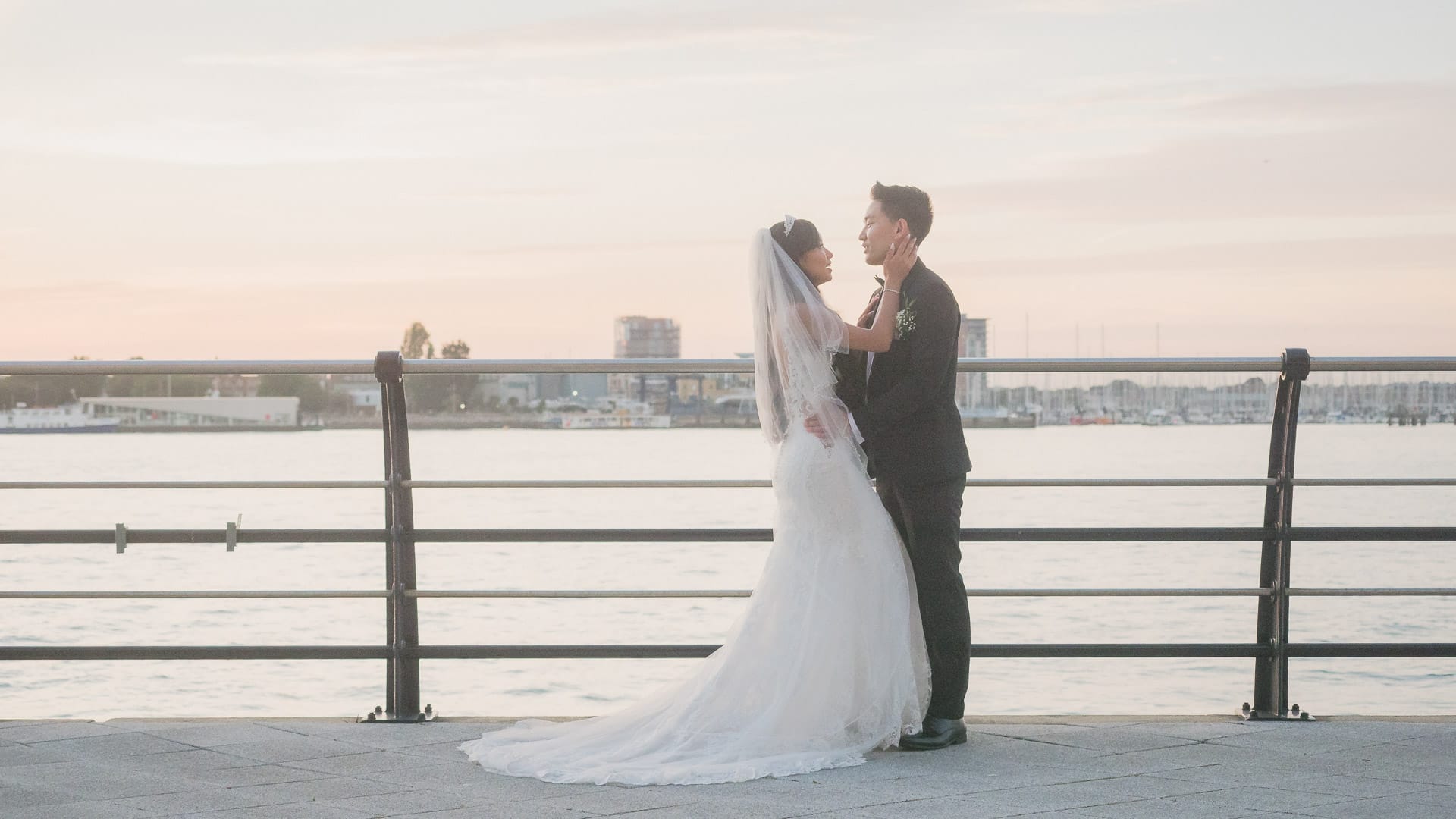 Bride and groom on a seaside promenade at sunset.