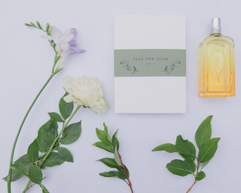 Flat lay of wedding stationery, l'Occitane perfume bottle and flowers